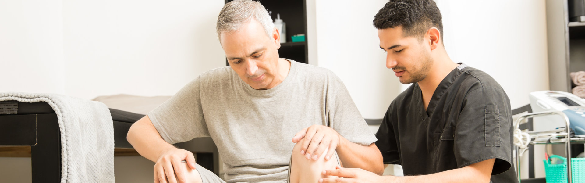 Therapist Assisting Mature Male Patient Sitting On Exercise Ball