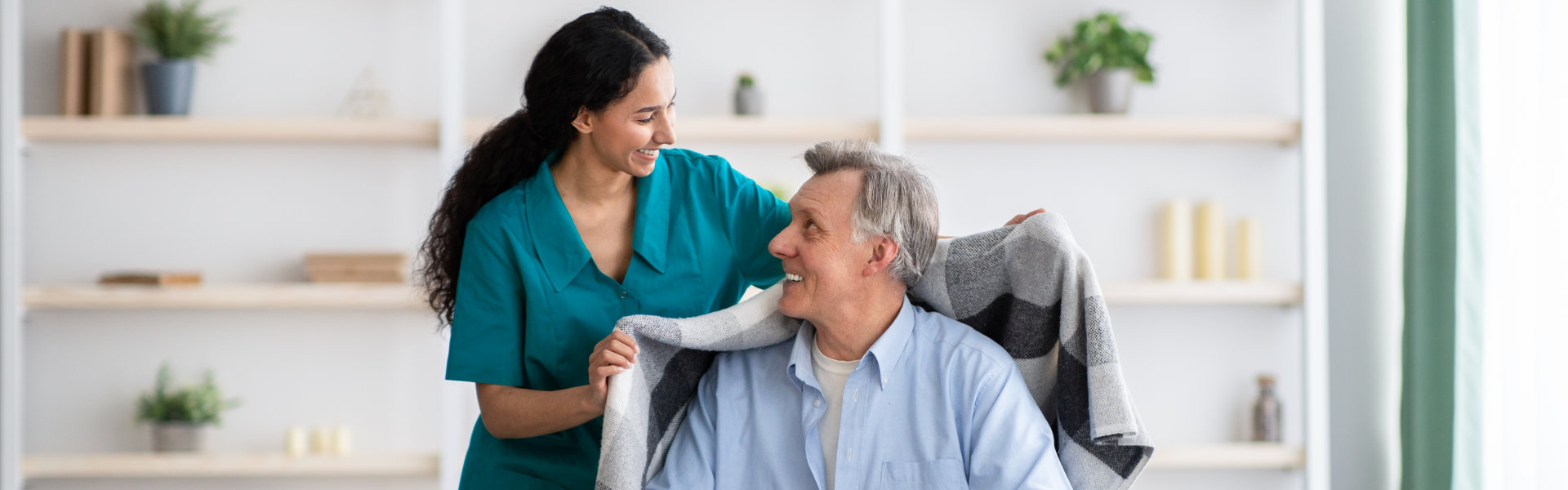 Young nurse covering a elderly man in wheelchair with warm plaid