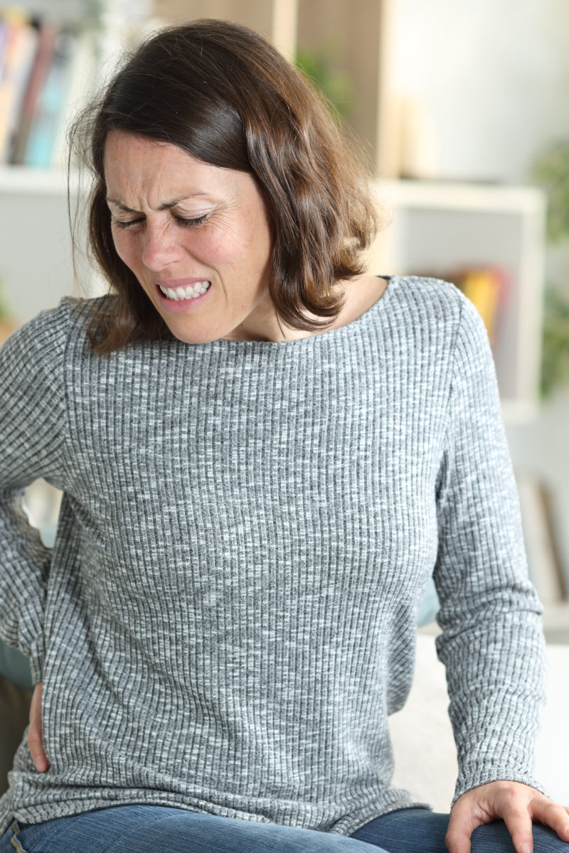 Middle age woman in pain suffering backache stting on a couch at home