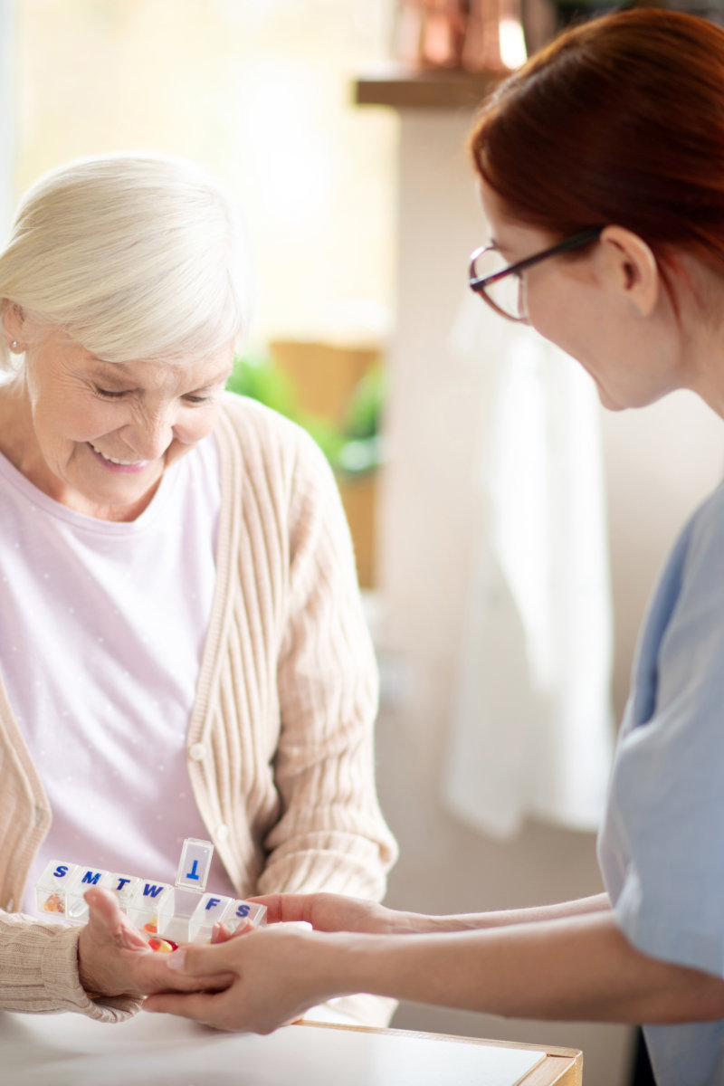 elderly woman taking vitamins standing near caregiver
