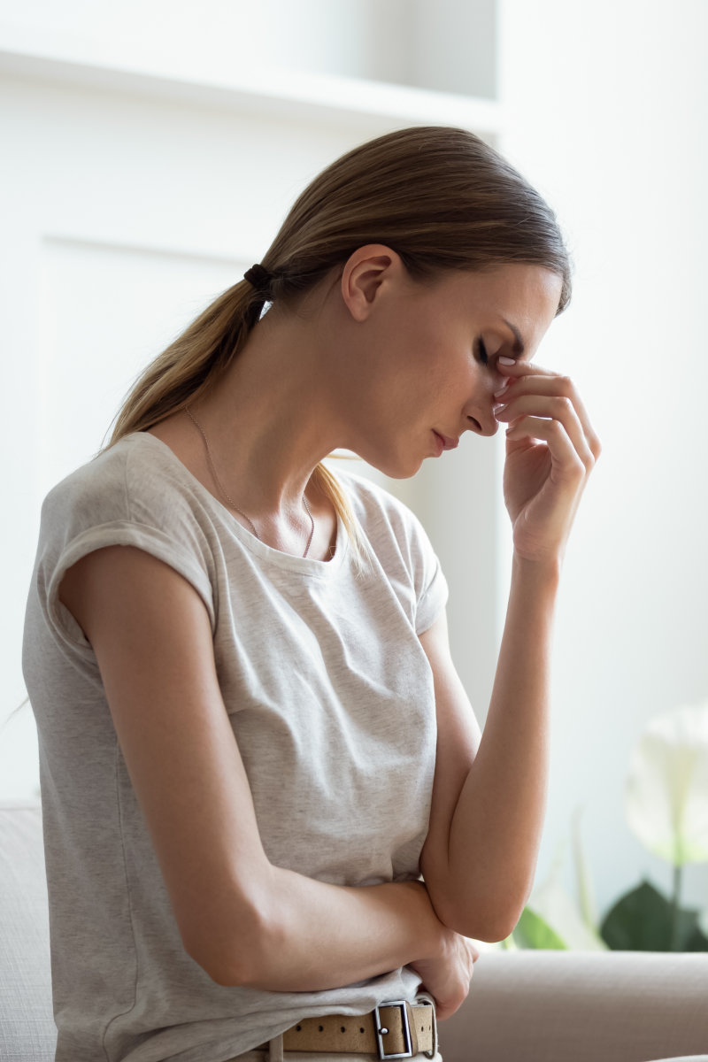 Unwell tired young woman sit on couch at home touch eyes suffer from migraine or sudden headache, exhausted millennial female feel unhealthy having dizziness or blurry vision